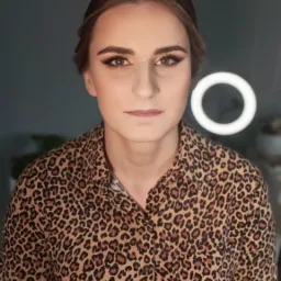 Portret kobiety z profesjonalnie wykonanym, wieczorowym make-upem oczu w odcieniach brązu i złota, ubrana w koszulę w panterkę, oświetlona lampą pierścieniową.