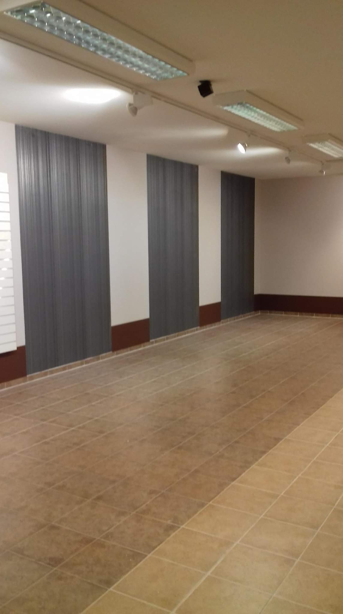 Wnętrze pomieszczenia po pracach wykończeniowych: brązowe płytki podłogowe ułożone w karo, pionowe panele ścienne w odcieniach szarości oddzielone białymi fragmentami ścian, brązowe listwy...