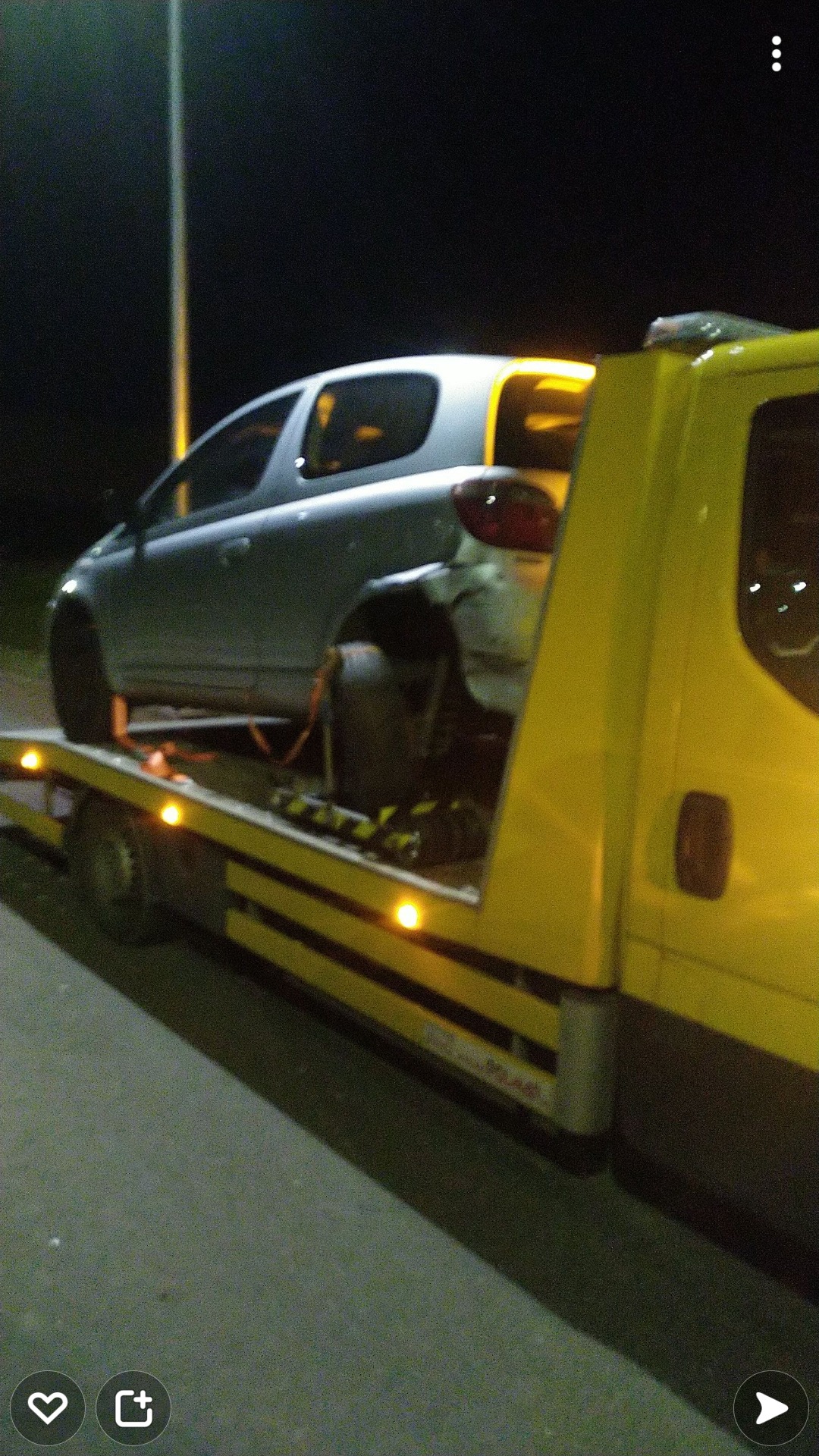 Uszkodzony, srebrny samochód osobowy załadowany na żółtą lawetę w Wałbrzychu, widoczne uszkodzenia z tyłu pojazdu, nocne oświetlenie uliczne w tle.