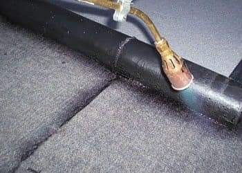 Palnik dekarski nagrzewa papę na dachu, widoczne stopienie materiału i połączenie z powierzchnią.