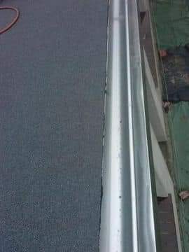 Szczegółowe ujęcie nowej, metalowej rynny zamontowanej na dachu pokrytym papą, widoczne połączenie z konstrukcją dachu i fragment węża na pierwszym planie.