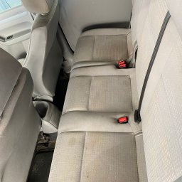 Pan Gąbka - Ręczna myjnia samochodowa - Wnętrze VW Caddy przed czyszczeniem: widoczne zabrudzenia na szarej tapicerce tylnej kanapy i podłodze, czerwone zapięcia pasów bezpieczeństwa.