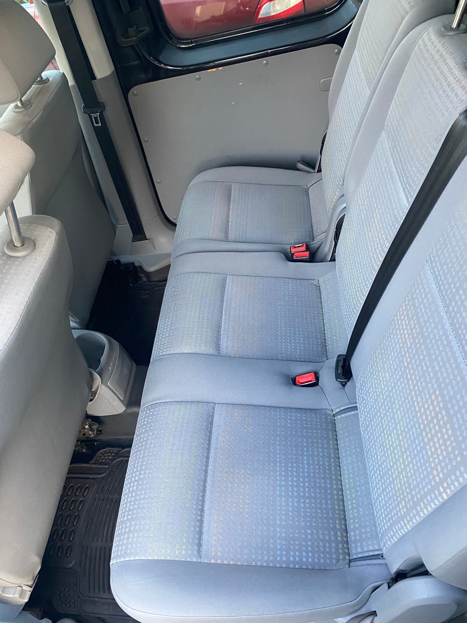 Wnętrze VW Caddy po czyszczeniu: jasnoszare fotele z wzorem w romby, widoczne pasy bezpieczeństwa i gumowe dywaniki pod siedzeniami.