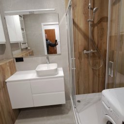 Renomex - Nowoczesna łazienka z kabiną prysznicową typu walk-in, umywalką nablatową na białej szafce i pralką. W lustrze odbija się osoba robiąca zdjęcie.