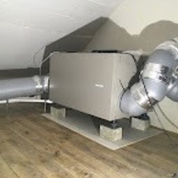 BCS Sp. z o.o. - Centrala wentylacyjna z podłączonymi przewodami na poddaszu, umieszczona na podkładkach z betonu komórkowego, widoczne skośne ściany i drewniana podłoga