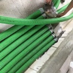 BCS Sp. z o.o. - Zielone, karbowane rury wentylacyjne ułożone równolegle na podłodze w trakcie montażu, widoczne ręce osoby zabezpieczającej połączenie taśmą.