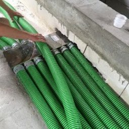 BCS Sp. z o.o. - Rząd zielonych, elastycznych przewodów wentylacyjnych ułożonych obok ściany z betonu komórkowego podczas instalacji.