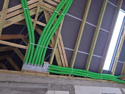 Zielone rury wentylacyjne prowadzone w przestrzeni poddasza z drewnianą konstrukcją, widoczne okno dachowe.