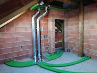 System kanałów wentylacyjnych z zielonymi rurami w surowym wnętrzu poddasza z ceglanymi ścianami i drewnianą konstrukcją dachu.