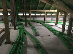 Układ zielonych rur wentylacyjnych na poddaszu, widoczne drewniane elementy konstrukcyjne dachu, szara betonowa podłoga.