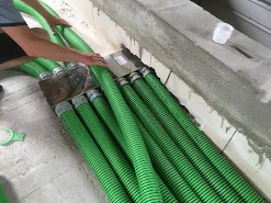 Rząd zielonych, elastycznych przewodów wentylacyjnych ułożonych obok ściany z betonu komórkowego podczas instalacji.