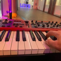 Cinnamon Live Cover Band - Dłoń grająca na czerwonym keyboardzie Nord, w tle sala z dekoracją LOVE podświetloną na niebiesko, prawdopodobnie podczas wesela.