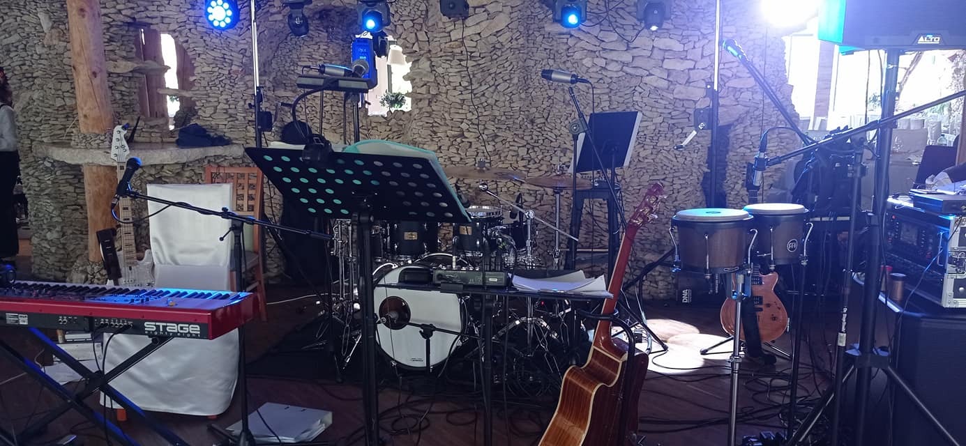 Scena z instrumentami muzycznymi: perkusja, gitary, keyboard Stage, mikrofony i oświetlenie, przygotowana do występu w kamiennej sali.