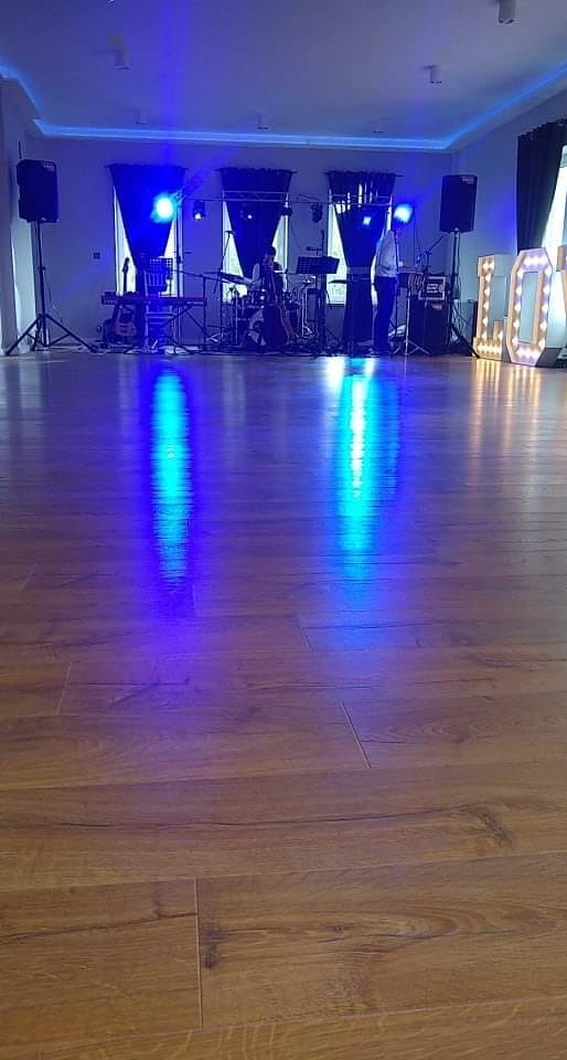 Zespół muzyczny na scenie z instrumentami, sprzętem nagłośnieniowym i dekoracyjnymi literami 'LOVE' z podświetleniem, widok z parkietu.