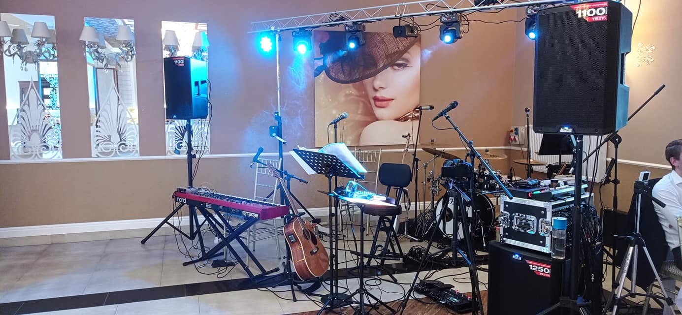 Scena z instrumentami muzycznymi i sprzętem nagłośnieniowym, przygotowana do występu, z plakatem kobiety w tle.