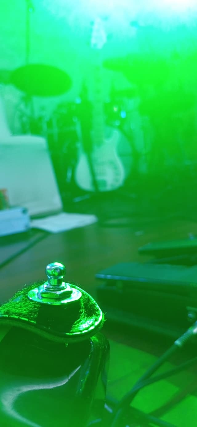 Efekt gitarowy podświetlony na zielono, w tle rozmyta gitara basowa i notatki.