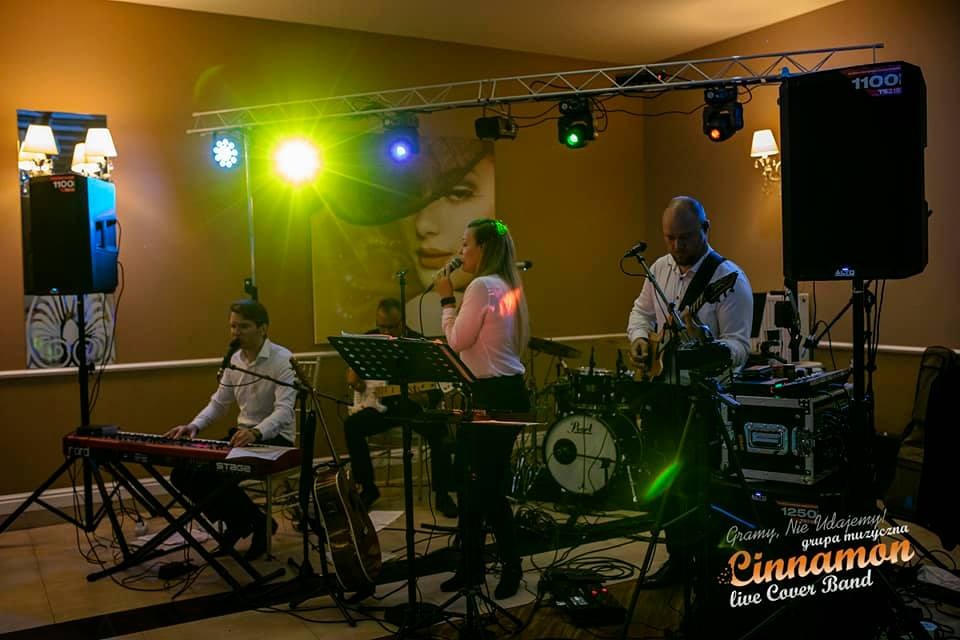 Zespół muzyczny Cinnamon gra na żywo w Częstochowie, piosenkarka śpiewa do mikrofonu, w tle gitarzysta, klawiszowiec i perkusista, oświetlenie sceniczne.