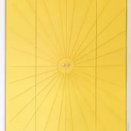 Żółta szafa wnękowa z dekoracyjnym wzorem promienistym i okrągłymi uchwytami na trzech frontach, widoczna na tle jasnej ściany i podłogi.