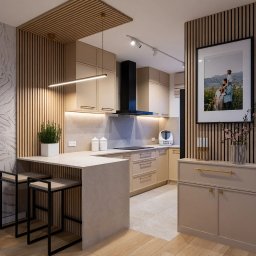 Dizaro Studio Projektowania Wnętrz - Beżowa kuchnia z drewnianymi lamelami, oświetleniem LED i wyspą z hokerami. Na ścianie dekoracyjny tynk i rodzinne zdjęcie w ramie. Nowoczesny design z akcentami natury.