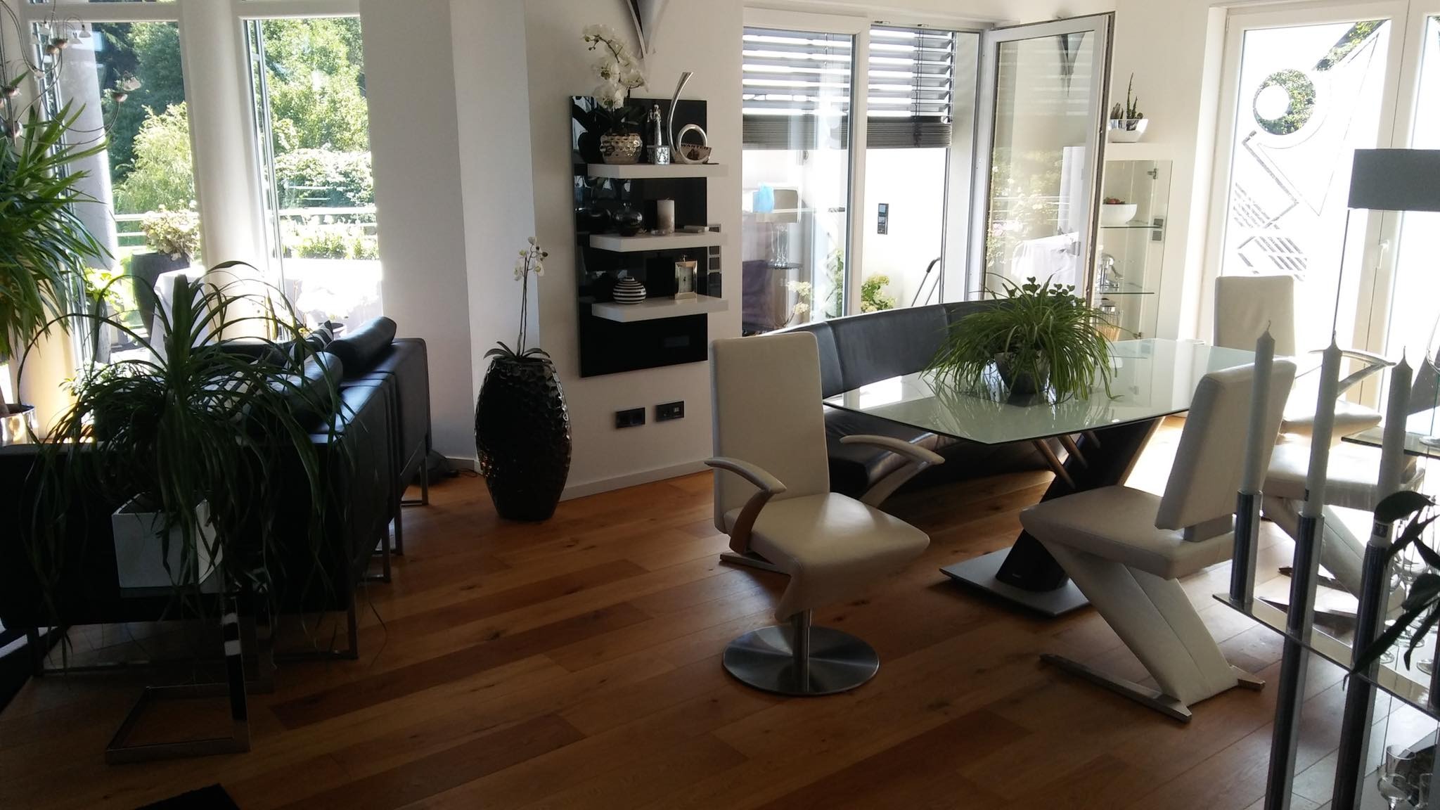 Jasne wnętrze salonu z drewnianą podłogą, nowoczesnymi meblami i dużymi oknami z widokiem na zieleń.