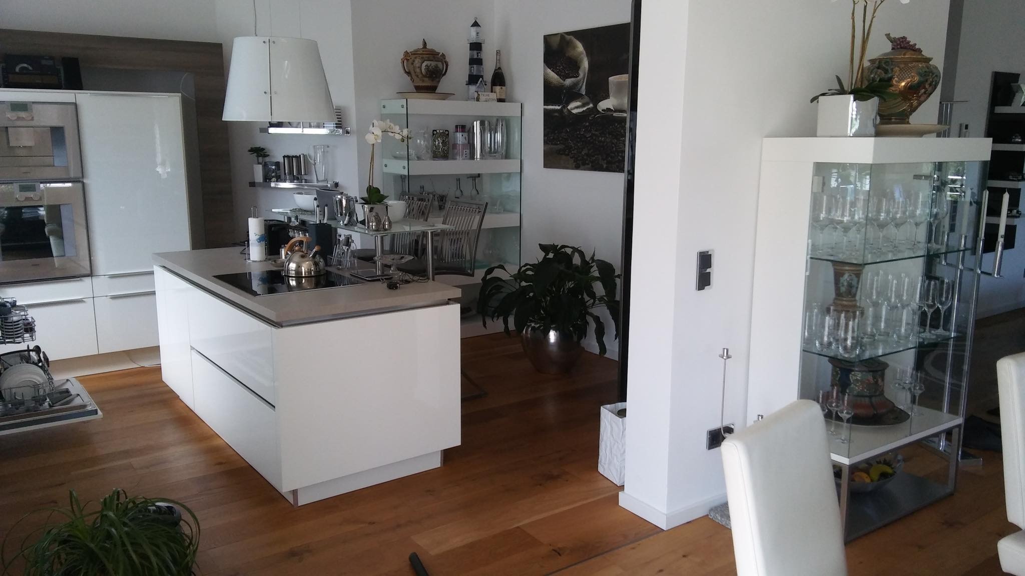 Jasna, nowoczesna kuchnia z wyspą, drewnianą podłogą i przeszkloną witryną z kieliszkami