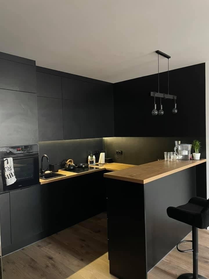 Nowoczesna kuchnia w czerni z drewnianym blatem, oświetlona wiszącymi lampami z żarówkami Edisona, z drewnianą podłogą i czarnym stołkiem barowym.