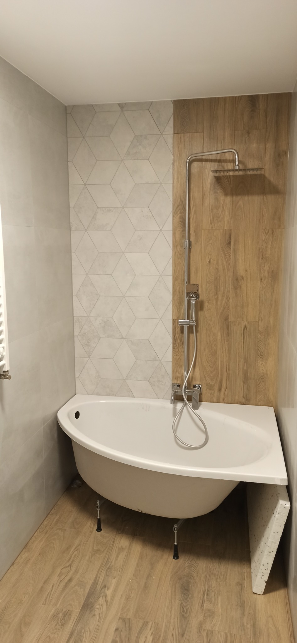 Nowoczesna łazienka z wolnostojącą wanną na nóżkach, drewnopodobnymi płytkami ściennymi i podłogowymi oraz geometrycznymi płytkami nad wanną.