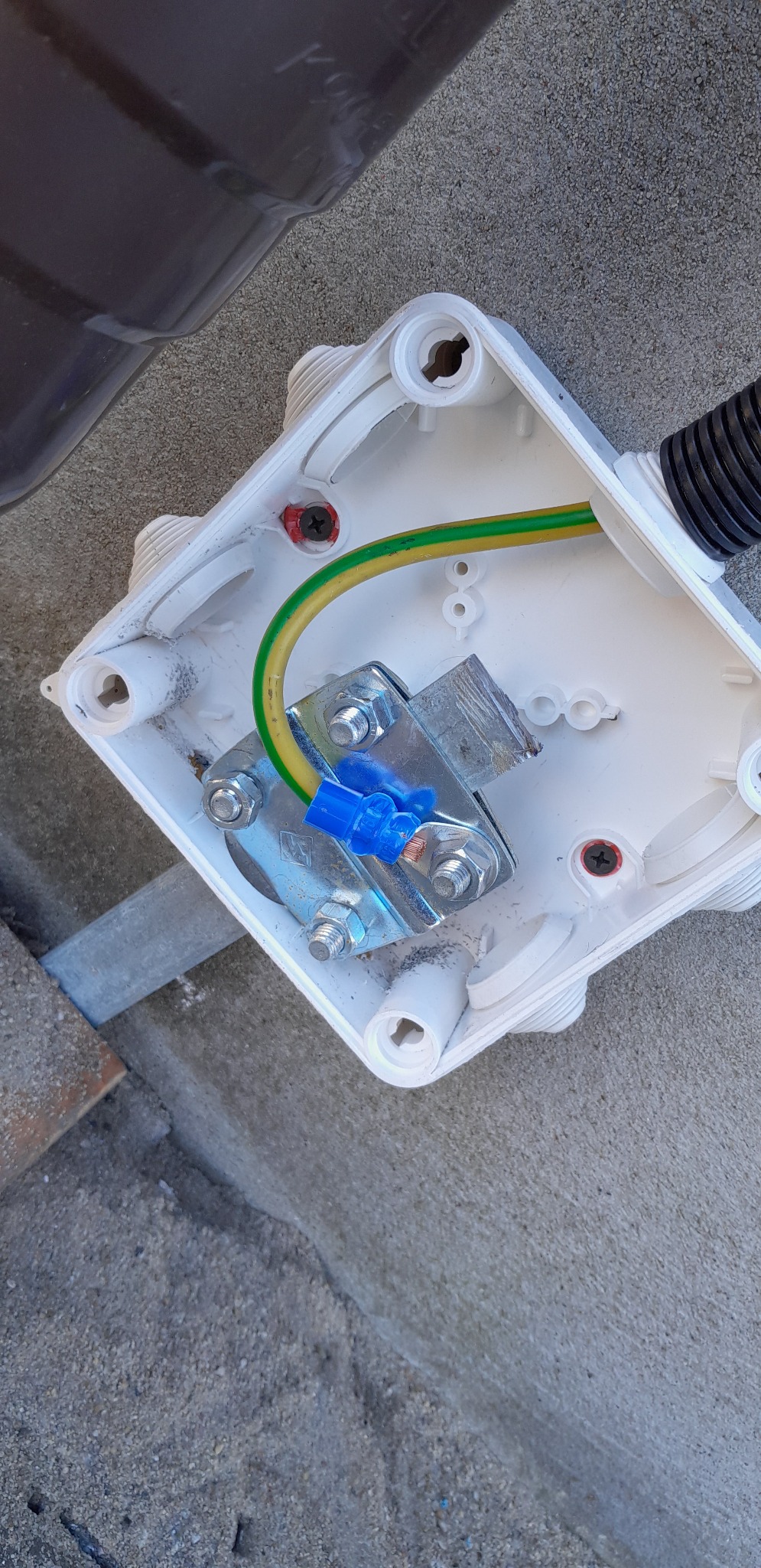 Otwarta puszka instalacyjna z widocznym przewodem uziemiającym (żółto-zielonym), złączką WAGO (niebieską) i metalową szyną montażową. W tle widoczny fragment elewacji.