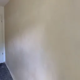 Ściana po nałożeniu gładzi, widoczne delikatne smugi i nierówności, przygotowana do dalszego malowania, zabezpieczona podłoga przy ścianie.