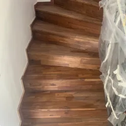 Ułożone drewniane schody spiralne z zabezpieczoną folią balustradą, widok z góry.