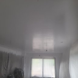 Emil Michalczak - Białe, świeżo pomalowane wnętrze z zabezpieczonymi folią ścianami i oknem, widoczne wiszące przewody elektryczne.