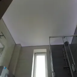 Biały, matowy sufit napinany w łazience z kabiną prysznicową i oknem, widok z dołu.