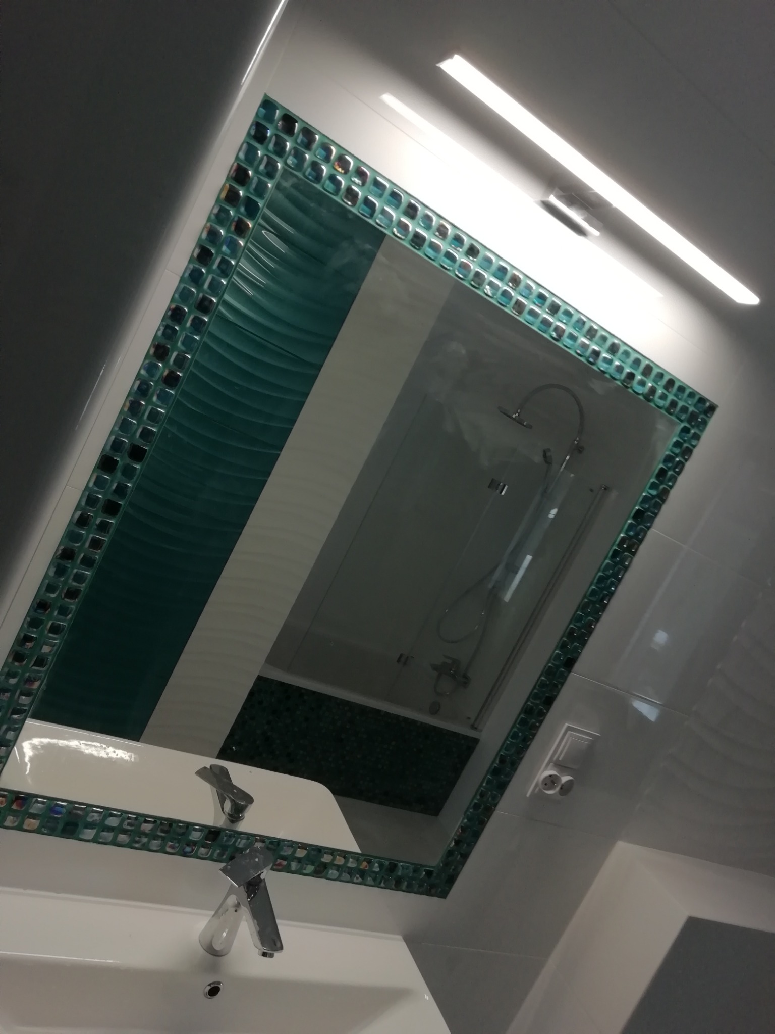 Wykończona łazienka z umywalką i lustrem w dekoracyjnej, mozaikowej ramie, odbijającym kabinę prysznicową z deszczownicą.