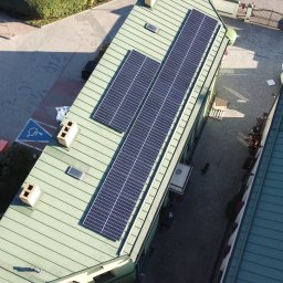 FORP Fotowoltaika i systemy grzewcze - Widok z góry na zielony dach budynku z zainstalowanymi panelami słonecznymi, widoczny fragment parkingu z symbolem osoby niepełnosprawnej oraz wewnętrzny dziedziniec z siedzącymi osobami.