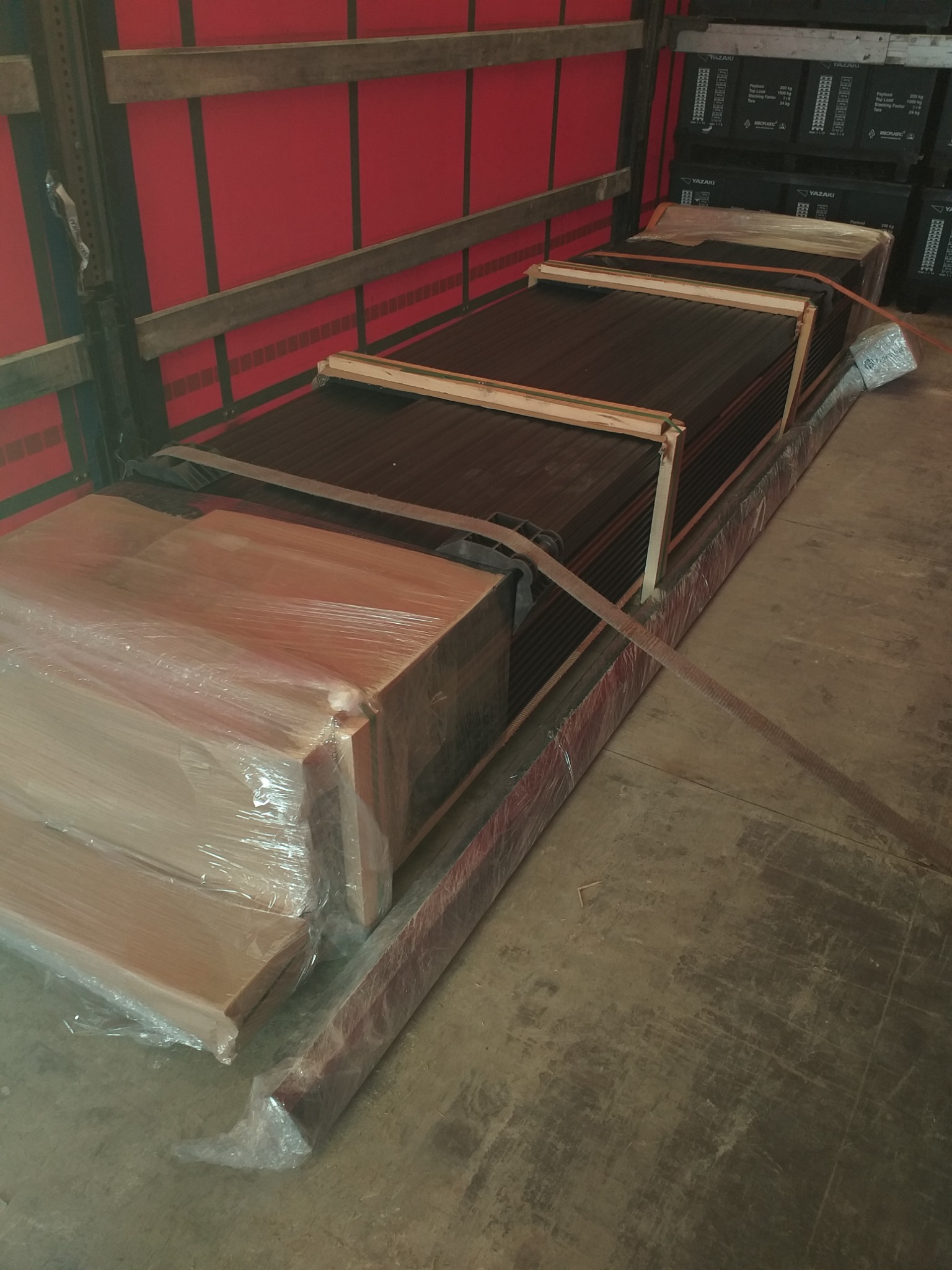 Transport kompozytowych desek tarasowych zabezpieczonych folią i drewnianymi przekładkami wewnątrz przyczepy ciężarówki.