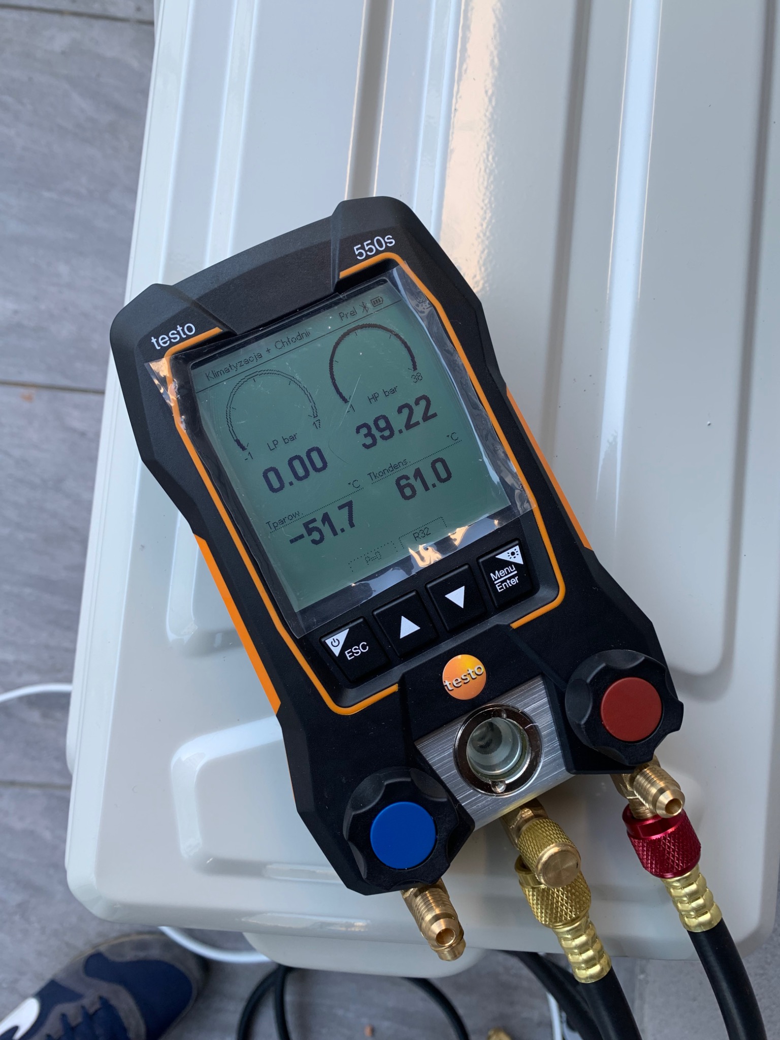 Cyfrowy manifold Testo 550s z podłączonymi przewodami pomiarowymi na tle białej obudowy klimatyzatora, wskazujący niskie ciśnienie 0.00 bar i temperaturę parowania -51.7 stopni Celsjusza.