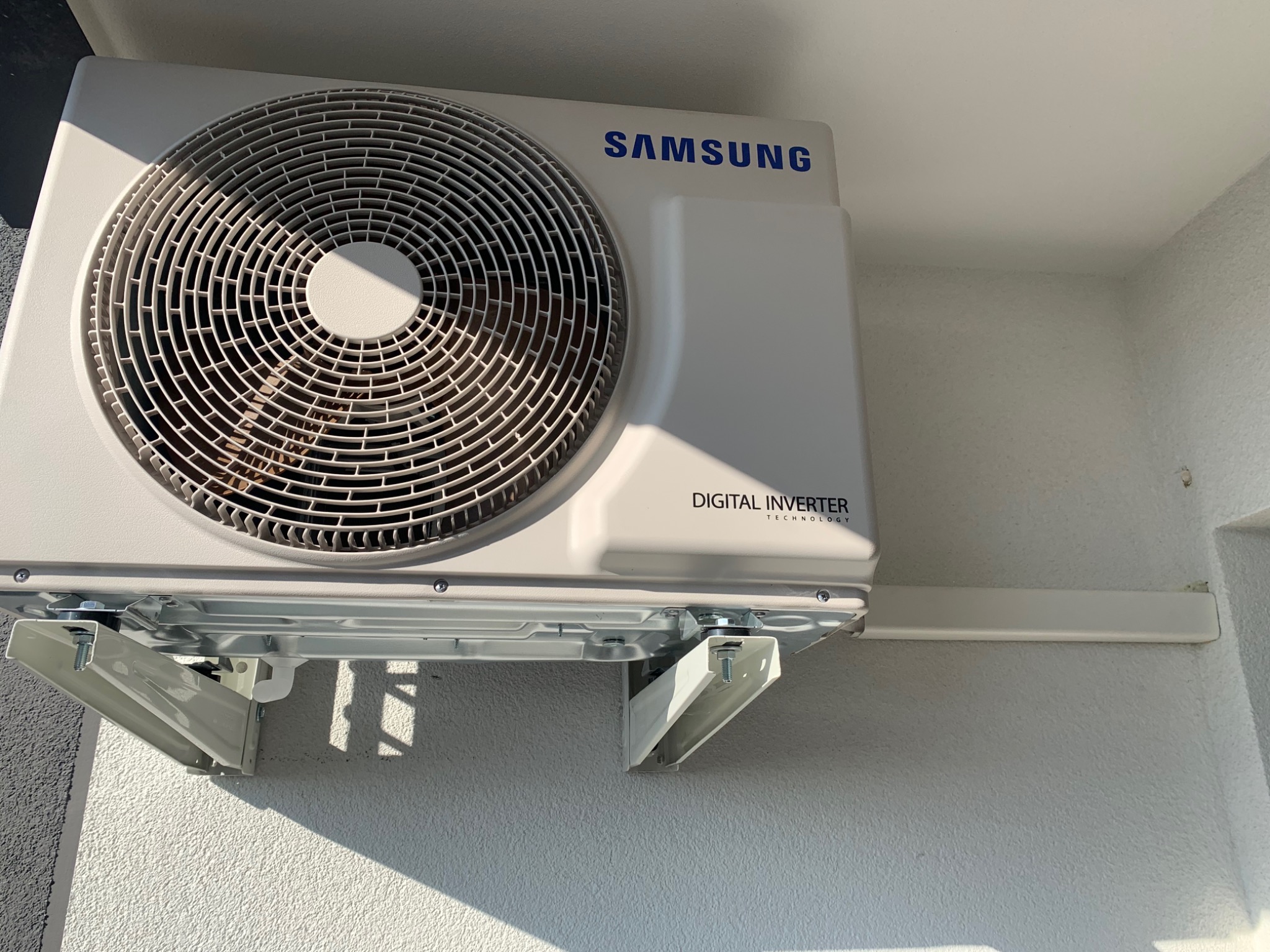 Zewnętrzna jednostka klimatyzacji Samsung Digital Inverter zamontowana na białej ścianie budynku za pomocą metalowych wsporników.
