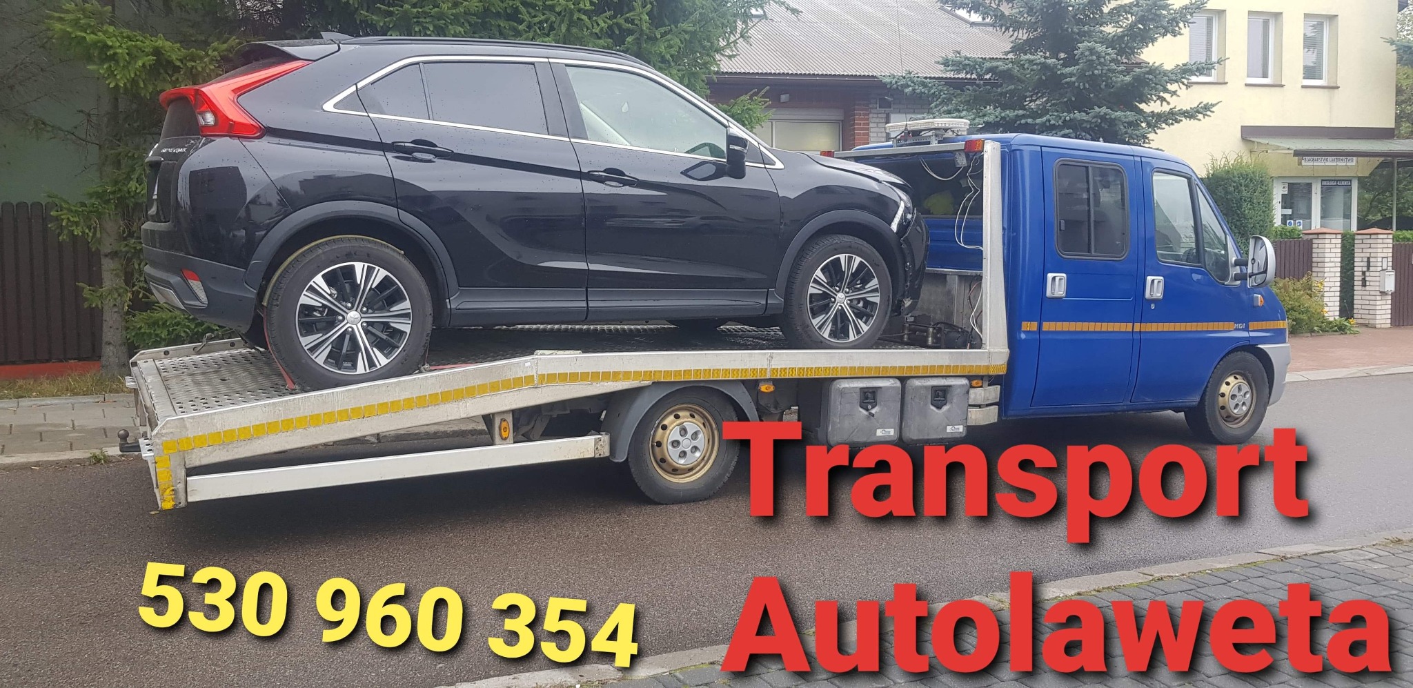 Czarny SUV Mitsubishi Eclipse Cross transportowany na niebieskiej lawecie na tle ulicy z budynkami i zielenią.
