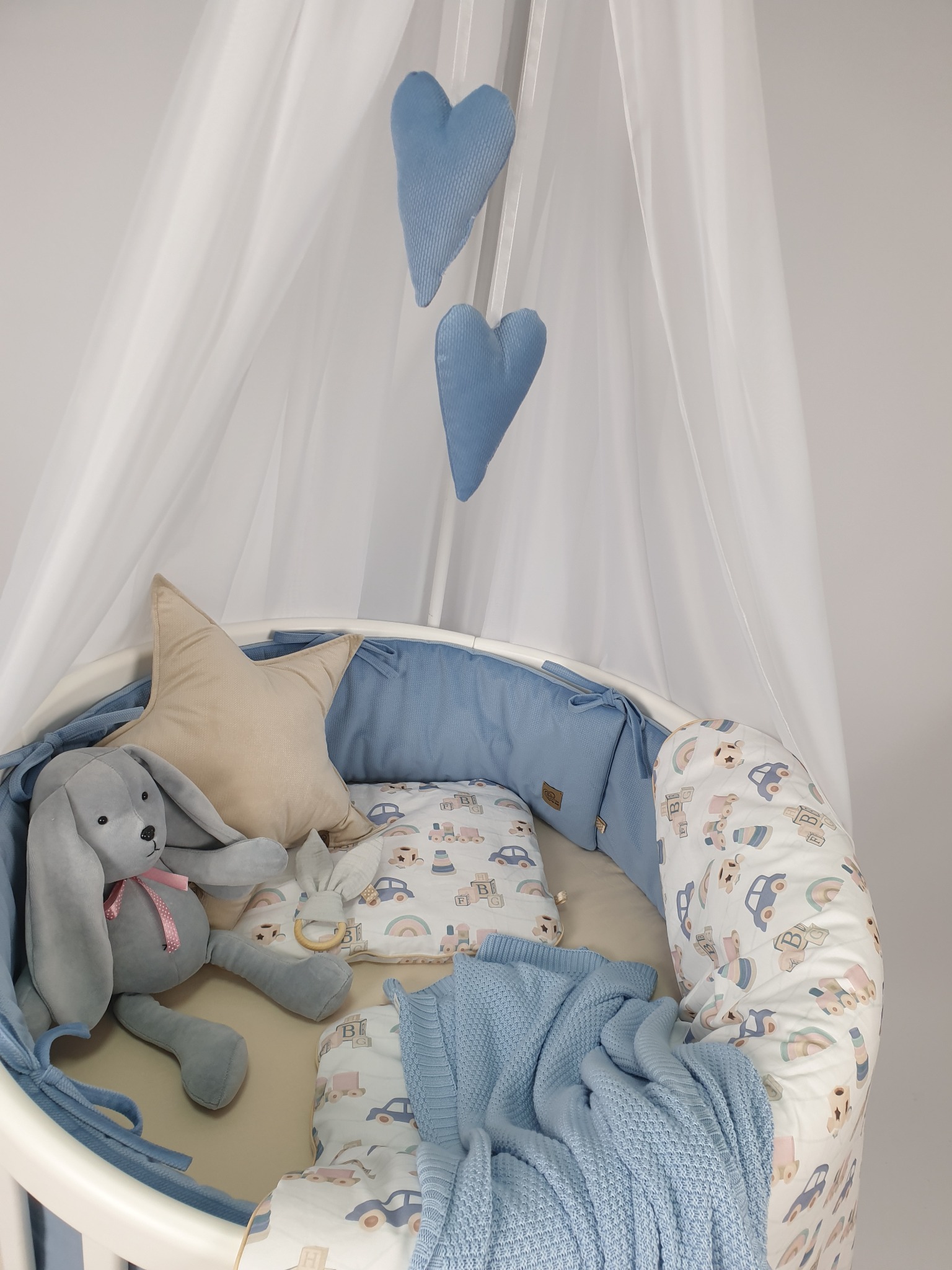 Błękitna wyprawka do łóżeczka dziecięcego: pluszowy królik, kocyk, poduszki w kształcie gwiazdy i serc, ochraniacz z motywem aut.