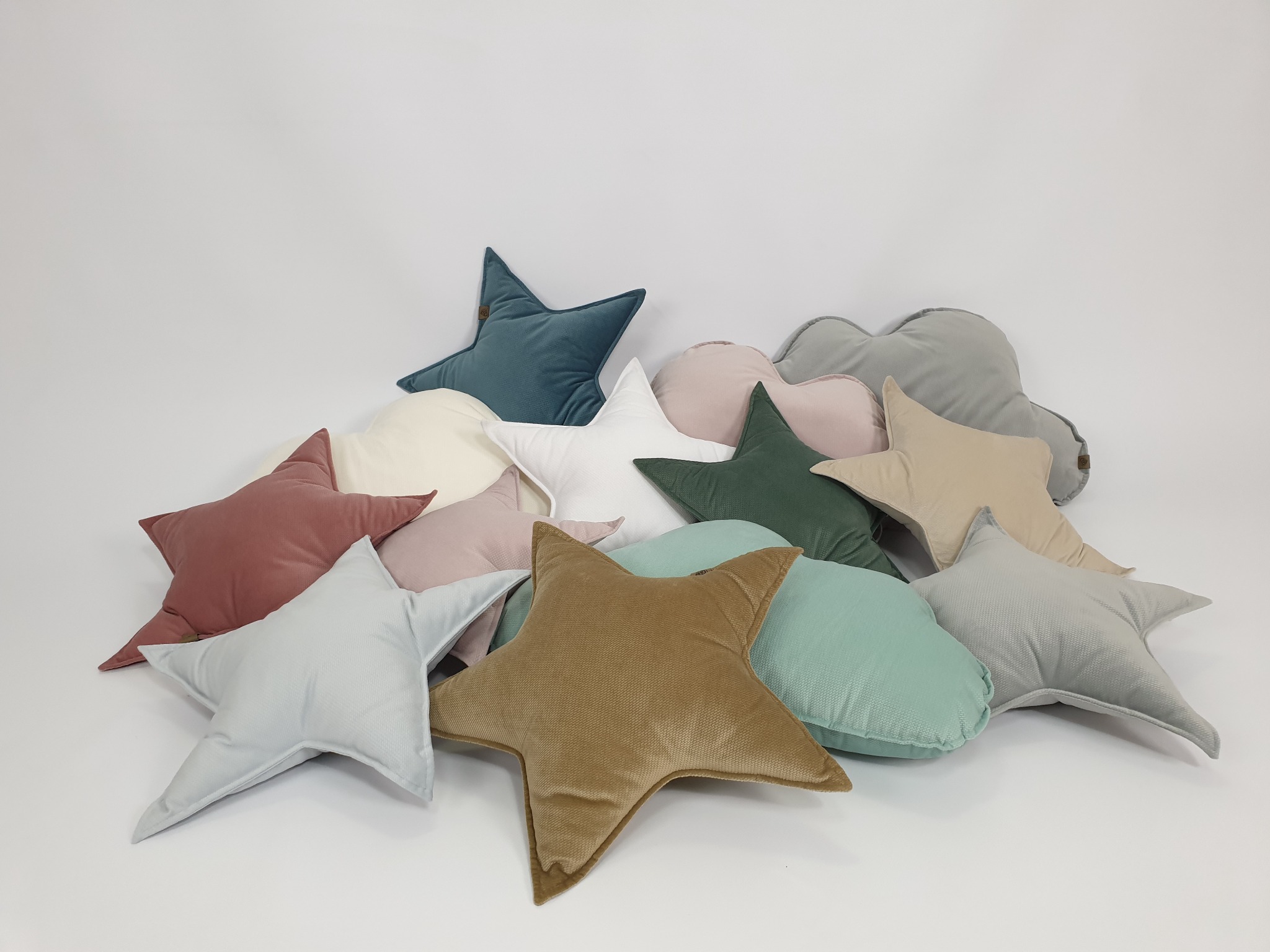 Stos poduszek dekoracyjnych: gwiazdy i chmurki w pastelowych kolorach na jasnym tle. Różnorodne faktury materiałów, miękkie wypełnienie, estetyczne wykończenie.