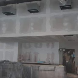 LUKAS USLUGI OGÓLNOBUDOWLANE - Wnętrze w trakcie prac wykończeniowych: ściany pokryte płytami gipsowo-kartonowymi, widoczny rusztowanie i elementy instalacji wentylacyjnej pod sufitem.