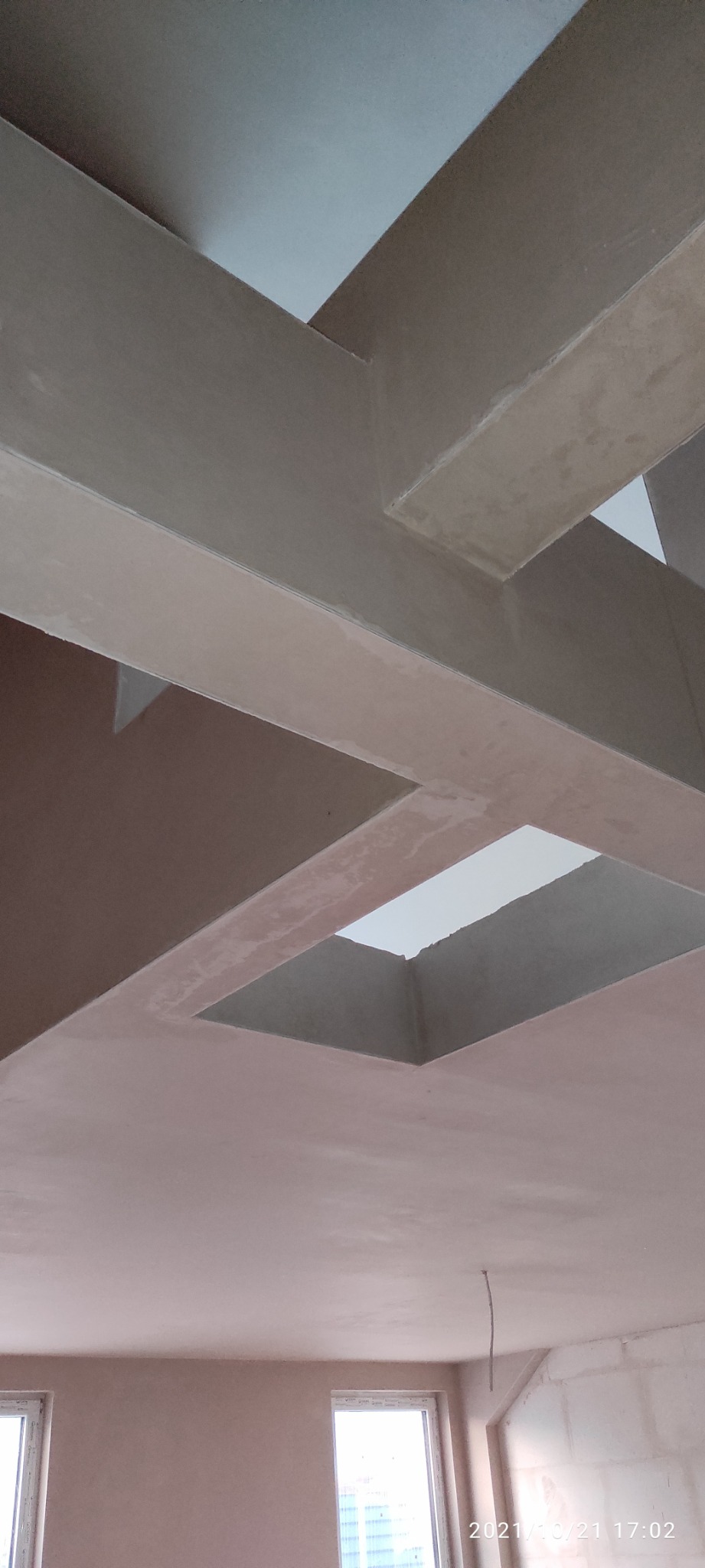 Sufit z nałożonymi tynkami maszynowymi, widoczne elementy konstrukcyjne tworzące geometryczny wzór, surowy stan wykończenia wnętrza.