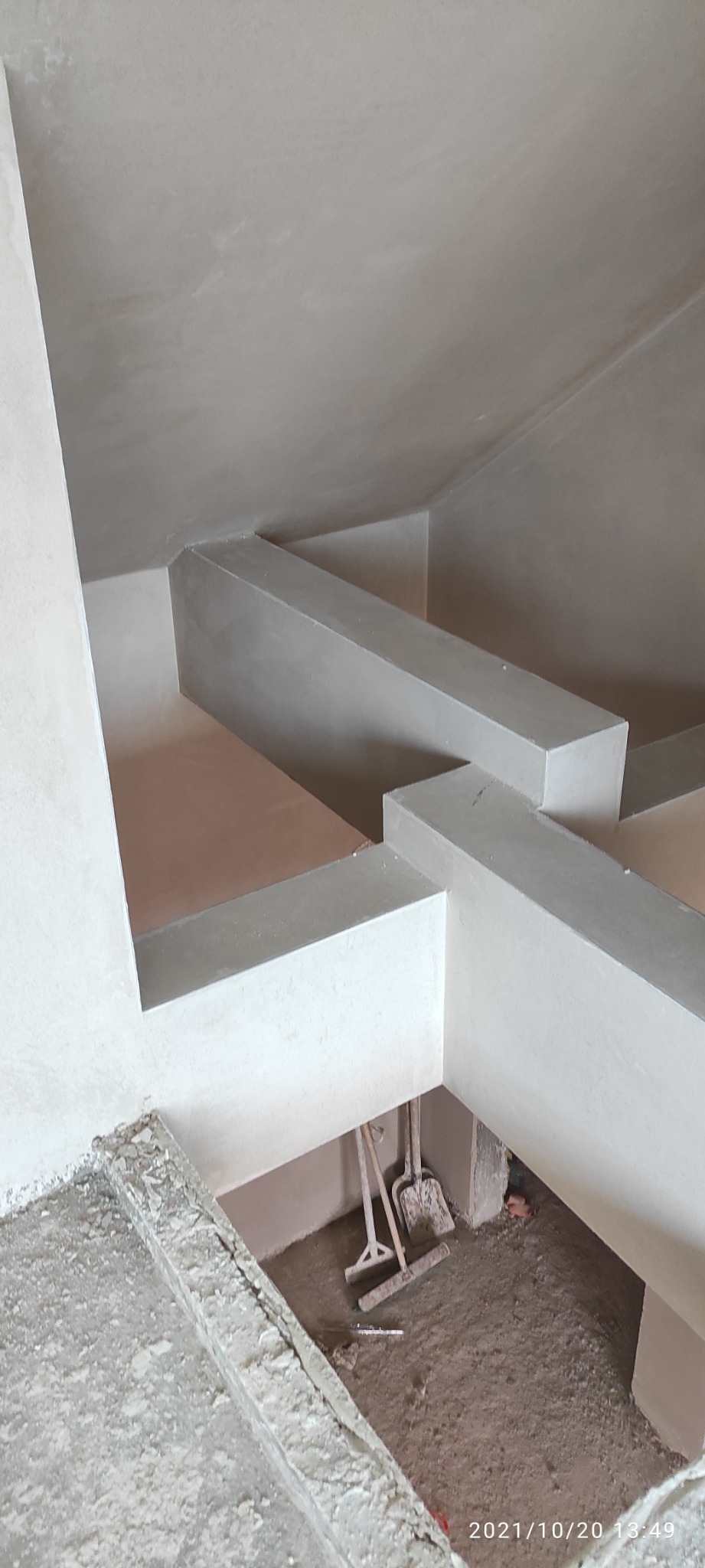 Świeżo otynkowane, surowe wnętrze z widocznymi belkami konstrukcyjnymi pod sufitem, narzędzia budowlane w tle.