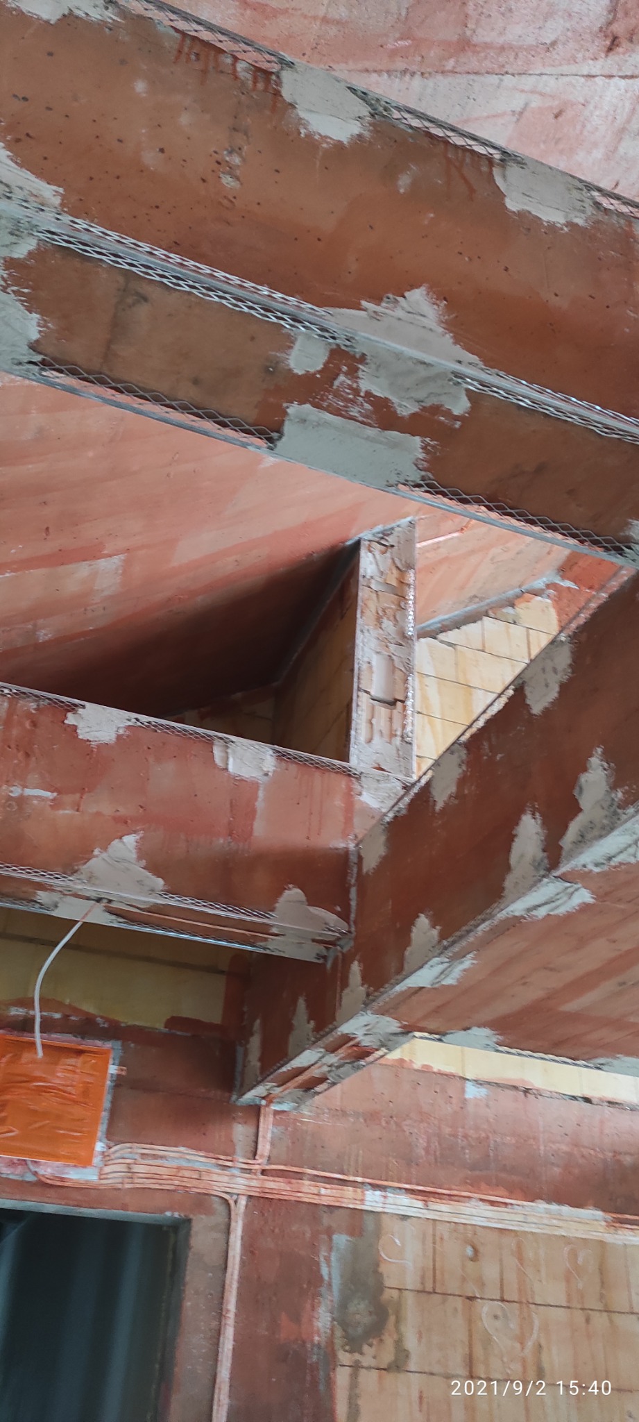 Wnętrze budynku w trakcie prac murarskich: ceglane ściany i strop z widoczną siatką zbrojeniową przygotowane do nałożenia tynku.