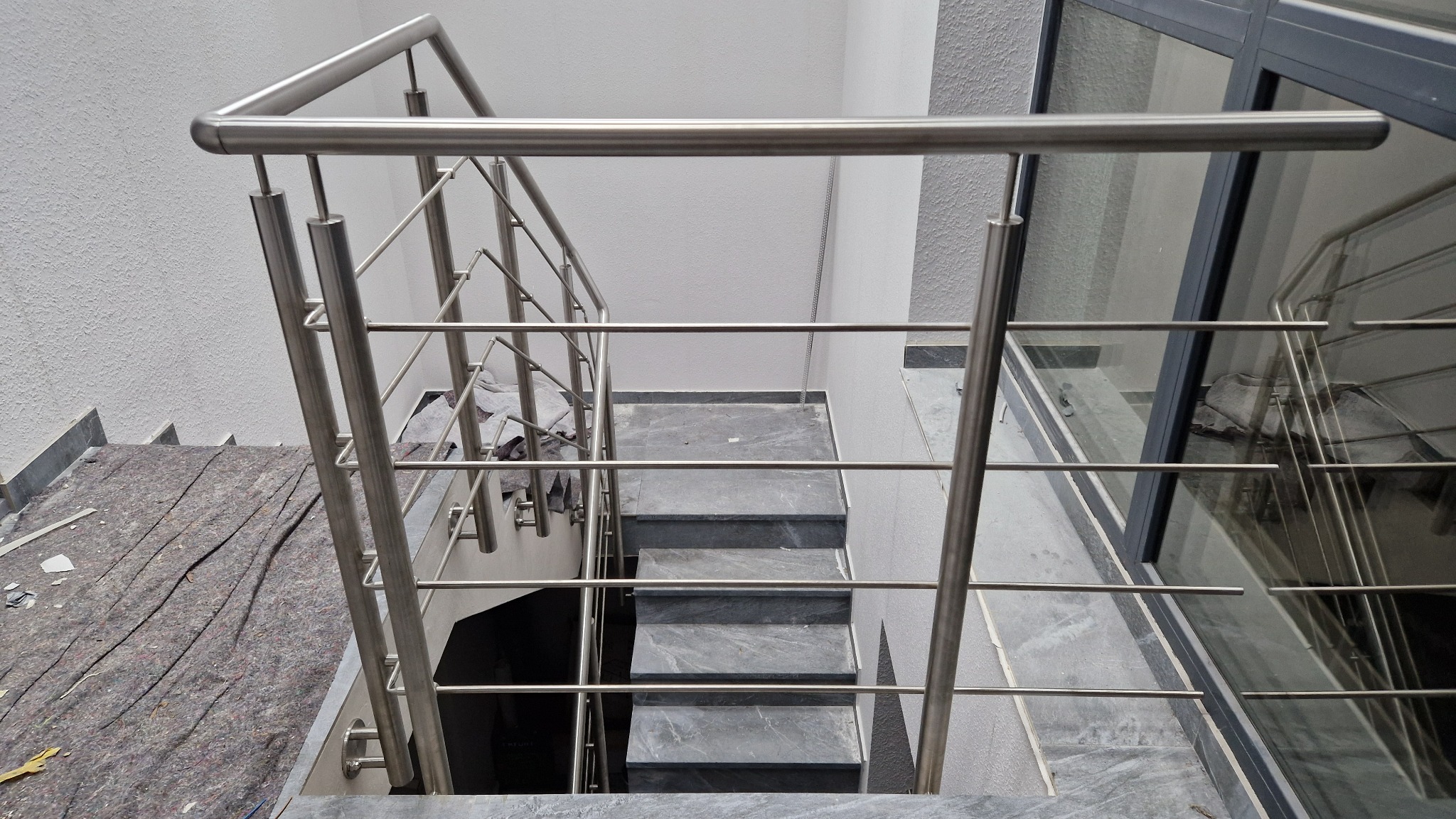 Widok z góry na schody z szarego kamienia z nowoczesną balustradą ze stali nierdzewnej, zabezpieczone podczas montażu szarą włókniną ochronną.