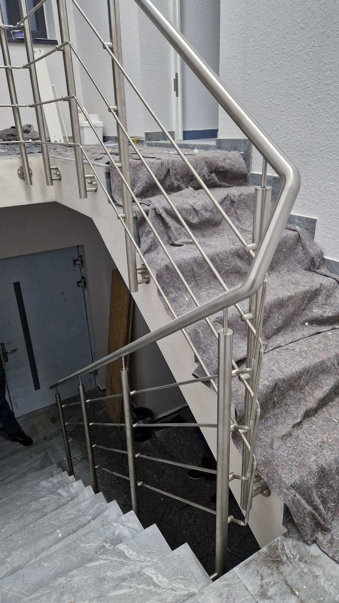 Nowoczesne schody z marmurowymi stopniami i balustradą ze stali nierdzewnej, zabezpieczone materiałem ochronnym podczas prac wykończeniowych.