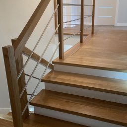 I WOOD DESIGN - Nowoczesne schody drewniane z dębowymi stopniami i balustradą z drewnianymi słupkami oraz poziomymi, metalowymi prętami, widoczne z dołu pod kątem, z białymi podstopnicami i wykończeniem podłogi...