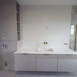 I WOOD DESIGN - Jasna łazienka z szafką pod umywalką z frezowanymi frontami, złotą armaturą i płytkami imitującymi marmur w strefie prysznica. Nowoczesny design.