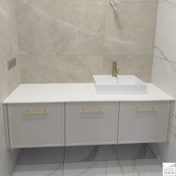 I WOOD DESIGN - Nowoczesna łazienka z białymi szafkami pod umywalką i złotymi uchwytami, na tle marmurowych płytek. Minimalistyczny design, ciepłe oświetlenie.