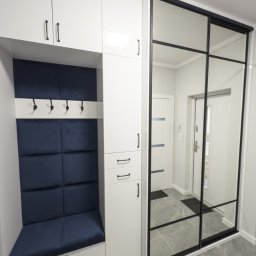 I WOOD DESIGN - Biała szafa wnękowa z siedziskiem i lustrzanymi drzwiami przesuwnymi w przedpokoju. Granatowe obicie siedziska i panelu ściennego. Minimalistyczny design.